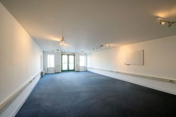 Lege kantoorruimte aan de Hoogte Kadijk met donkerblauw tapijt, witte muren en een whiteboard aan de wand.